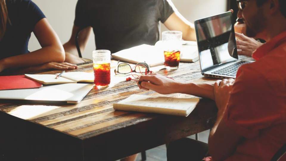 Photo éditoriale : une équipe réunie autour d'une table de travail en bois, ordinateur portable ouvert, lumière naturelle